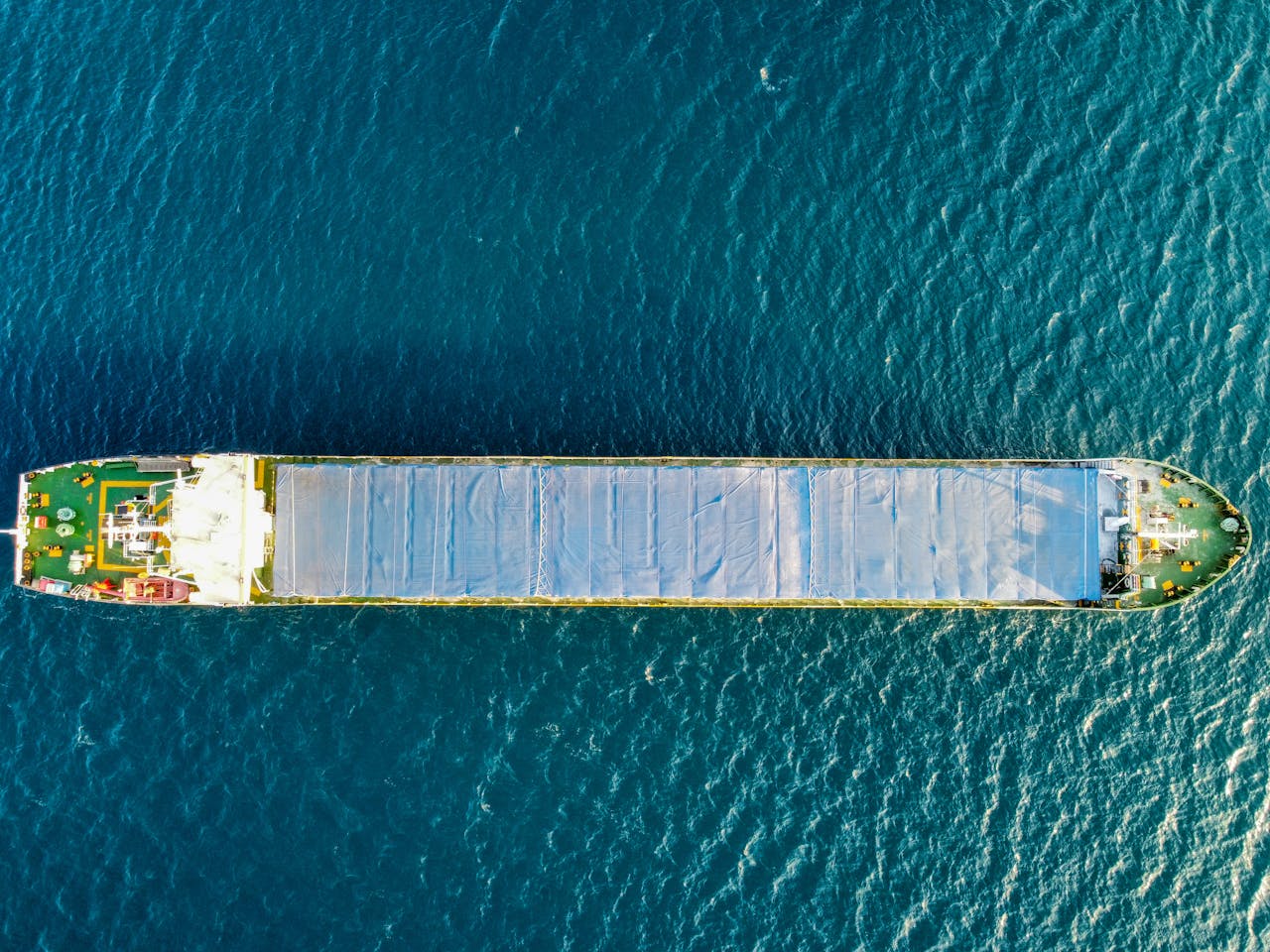 about-us Top-down aerial view of a cargo ship navigating the open sea under clear skies.