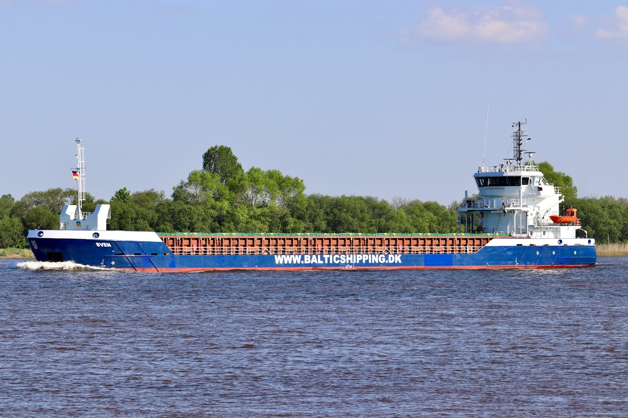 services-04 A blue cargo ship sails near a green coastline under a clear sky. Ideal for logistics themes.